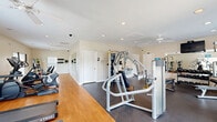 Located at 4632 Still Meadow Dr in Wilmington, NC, this fitness center offers a thoughtfully designed, single-floor exercise space that accommodates a comprehensive range of workout options. The layout is divided into distinct functional zones, with warm hardwood flooring in the cardio area and durable rubber flooring underfoot in the strength training sections, providing both comfort and safety.

The cardio zone is well-stocked with treadmills, elliptical machines, a stationary bike, a stair climber, and a rowing machine, all positioned near windows that let in generous natural light and offer views of the surrounding greenery. A wall-mounted TV supports entertainment during workouts.

The strength training area features a cable machine, a multi-function weight station, a dumbbell rack, and a medicine ball rack with a full color-coded set. Large mirrors line the walls, enhancing the sense of space and aiding in form checks during exercise.

Ceiling fans are distributed throughout the space, ensuring consistent airflow and comfort. Recessed lighting supplements natural illumination for a bright, energizing atmosphere. A water station and sanitation supplies are conveniently accessible. Glass-paned doors provide an additional connection to the outdoors, rounding out a clean, well-maintained environment suited for a full-body fitness routine.
