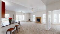 This single-story residence offers a well-designed open floor plan that seamlessly connects the main living areas. The expansive living room is a central highlight, featuring a tile-surround fireplace flanked by windows that invite natural light throughout the day. A ceiling fan overhead adds both function and comfort to the generous carpeted space. The vaulted ceiling detail in the living area contributes to an airy, open atmosphere.

The kitchen is equipped with warm-toned wooden cabinetry, dark countertops, and a full suite of stainless steel appliances, including a range, microwave, and refrigerator. A peninsula with an integrated sink and bar seating provides additional workspace and a casual dining option. Tile flooring runs throughout the kitchen and adjoining areas.

Bedrooms are carpeted and well-proportioned, with at least one featuring access to a walk-in closet with built-in shelving. The bathrooms are finished with tile flooring, warm wood vanities, and white countertops. An in-unit laundry area with washer and dryer hookups adds everyday convenience. The entry foyer, with its dark front door and sidelight window, provides a welcoming transition into the home.