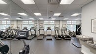 Located at 740 Smallwood Drive in Raleigh, NC, the Wedgwood Fitness Center is a thoughtfully designed, single-floor facility that provides residents with a comprehensive workout environment. The main exercise area is bright and open, featuring a drop-panel ceiling with recessed fluorescent lighting and large windows along the perimeter walls that allow generous natural light and views of the surrounding greenery, creating an inviting atmosphere for exercise.

The cardio zone is well-stocked with multiple treadmills, elliptical trainers, and stationary and recumbent bikes, offering a variety of options for aerobic training. A multi-station cable and weight machine provides a dedicated space for strength training, while a separate free weights section includes dual dumbbell racks with benches and exercise mats, catering to a range of fitness routines. Floor-to-ceiling mirrors are strategically placed throughout the space, enhancing the sense of openness while allowing users to monitor their form.

The facility includes a closet for storage and a full bathroom for convenience. A water fountain station is also available near the entry area. The durable rubber flooring throughout the gym ensures safety and comfort during workouts. Accessed through a glass-door entrance adjacent to the Wedgwood Business Center, this fitness space is a functional and well-maintained amenity.