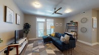 This single-floor residence offers a well-designed layout with distinct living, dining, kitchen, and sleeping areas. The open-concept kitchen is a standout feature, equipped with stainless steel appliances, a two-tone cabinet scheme pairing white upper cabinets with dark lower cabinets, subway tile backsplash, and a central island with pendant lighting and bar seating. Light wood-style flooring runs throughout the kitchen and dining area, which includes space for a dining table. The living room is generously proportioned, featuring wood-style flooring, a ceiling fan, textured ceiling, and French doors leading to a private balcony, allowing natural light to fill the space. Multiple bedrooms are finished with neutral-toned carpet and windows with blinds providing outdoor views. The bathrooms are clean and functional, featuring large-format tile flooring, dark espresso vanity cabinetry, light countertops, large mirrors, and brushed nickel fixtures. One bathroom includes a soaking tub and separate shower area. Neutral warm-gray walls throughout the unit create a cohesive and understated aesthetic.