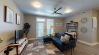 This single-floor residence offers a well-designed layout with distinct living, dining, kitchen, and sleeping areas. The open-concept kitchen is a standout feature, equipped with stainless steel appliances, a two-tone cabinet scheme pairing white upper cabinets with dark lower cabinets, subway tile backsplash, and a central island with pendant lighting and bar seating. Light wood-style flooring runs throughout the kitchen and dining area, which includes space for a dining table. The living room is generously proportioned, featuring wood-style flooring, a ceiling fan, textured ceiling, and French doors leading to a private balcony, allowing natural light to fill the space. Multiple bedrooms are finished with neutral-toned carpet and windows with blinds providing outdoor views. The bathrooms are clean and functional, featuring large-format tile flooring, dark espresso vanity cabinetry, light countertops, large mirrors, and brushed nickel fixtures. One bathroom includes a soaking tub and separate shower area. Neutral warm-gray walls throughout the unit create a cohesive and understated aesthetic.