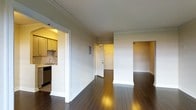 This single-floor residence offers a cohesive and functional layout highlighted by rich, dark hardwood floors that run throughout the main living areas, adding warmth and elegance to the space. Crown molding accents the ceilings, lending a classic architectural detail that elevates the overall aesthetic.

The open living area flows naturally toward a dedicated entryway, creating a welcoming sense of arrival. A partial wall defines the space without fully closing it off, maintaining an airy, connected feel between rooms. The entryway features a solid front door and leads seamlessly into the main living zone.

Adjacent to the living area, the kitchen is thoughtfully positioned for convenience. It features light-toned cabinetry, a tile backsplash, a stainless steel sink, and under-cabinet lighting that casts a warm glow over the workspace. Stainless steel appliances, including a dishwasher, complete the kitchen's practical setup.

The neutral wall tones throughout the residence complement both the flooring and trim work, creating a balanced and versatile palette. The layout also includes an additional alcove or room off the main living space, offering flexible use as a bedroom, office, or den. Overall, the space presents a clean, classic design with thoughtful architectural finishes.