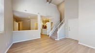 This two-story home is thoughtfully designed to maximize space and natural light across two well-proportioned floors. The main level opens into a striking living room distinguished by soaring vaulted ceilings, a ceiling fan, and multiple windows with blinds that flood the space with natural light. Light wood-tone flooring flows seamlessly throughout the first floor, complementing the neutral, warm-toned walls. A fireplace adds a functional focal point to the living area, while an open pass-through connects to the kitchen. The kitchen features white shaker cabinetry, stainless steel appliances including a range and microwave, a subway tile backsplash, and access to an additional closet for pantry or storage use. A staircase with a white banister leads to the upper level. The second floor hosts the spacious primary bedroom, carpeted for comfort and equipped with a ceiling fan, a generous window with outdoor views, and direct access to a large walk-in closet outfitted with wire shelving on multiple walls. The bathrooms are clean and well-finished, one featuring a soaking tub with subway tile surround and chrome fixtures. A hallway and an additional closet round out the upper floor, providing ample organization and storage throughout the home.