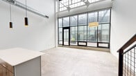 This distinctive two-story loft blends industrial character with modern residential living across two well-proportioned floors. The main level is anchored by a dramatic open living and kitchen area with soaring ceilings and an expansive wall of steel-framed, floor-to-ceiling windows that flood the space with natural light and offer views of an interior courtyard. The kitchen features white cabinetry with a subway tile backsplash, stainless steel appliances, and a peninsula counter. Polished concrete floors and exposed ductwork underscore the industrial aesthetic throughout the main level. A striking open-tread wood staircase with a black metal railing connects the two floors. The lower level also includes bedrooms with warm wood plank ceilings, a ceiling fan, and a full bathroom with a tub/shower combination and warm-toned concrete flooring. Upstairs, the bedrooms offer elevated ceilings, natural pine hardwood floors, and access to a dedicated closet. The upper-level bathroom mirrors the clean, minimal design with a full tub/shower and wood flooring. Throughout, the space maintains a consistent palette of crisp white walls, natural wood accents, and industrial finishes, creating a sophisticated and versatile environment.