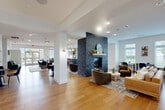 Located at 346 Turnpike Rd in Westborough, MA, this thoughtfully designed single-floor amenity space offers a generous and versatile layout across its expansive square footage. The interior is unified by warm-toned hardwood flooring that flows seamlessly throughout, complemented by crisp white walls and recessed lighting that create a bright, welcoming atmosphere.

The centerpiece of the space is a dramatic floor-to-ceiling stacked stone fireplace with a wood mantel, anchoring the main lounge area where curved upholstered seating and a round coffee table invite relaxed gatherings. Adjacent to the lounge, a sleek bar area features a dark-toned counter with leather bar stools, globe pendant lighting, and built-in shelving, making it ideal for social events.

A co-working zone is defined by a stylish wood slat partition screen, offering semi-private workstations with ample natural light from large windows overlooking the outdoors. A dedicated quiet room houses a modern freestanding phone booth alongside a round dining table and chairs for focused work or small meetings.

A cozy lounge nook features a plush sectional sofa, small bistro tables, and a decorative landscape mural wall paired with a compact kitchenette. French glass doors and open sightlines throughout the space enhance connectivity between zones while maintaining a cohesive, sophisticated aesthetic.