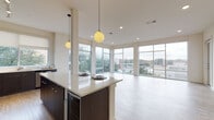 This contemporary single-floor residence showcases a thoughtfully designed open-concept layout that seamlessly connects the kitchen and living areas. The kitchen is a standout feature, equipped with stainless steel appliances, sleek dark cabinetry, light quartz countertops, and a generous island with a built-in wine cooler. Globe pendant lights hang overhead, adding a modern touch, while large floor-to-ceiling windows and a corner glass wall flood the space with natural light and offer sweeping outdoor views. Light wood-style flooring runs throughout the main living area, enhancing the bright and airy ambiance. The bedrooms are carpeted for comfort, each featuring ceiling fans and oversized sliding glass doors that open to private balconies with scenic tree and neighborhood views. Closets are outfitted with adjustable wire shelving systems, providing versatile and organized storage. The bathrooms are elegantly finished with large-format marble-patterned tile flooring and wall surrounds. The primary bath includes both a soaking tub and a separate glass-enclosed shower, paired with white cabinetry and a well-lit vanity mirror. A secondary bathroom mirrors the same refined aesthetic. Overall, the space combines modern finishes with functional design for a polished and comfortable living environment.