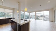 This contemporary single-floor residence showcases a thoughtfully designed open-concept layout that seamlessly connects the kitchen and living areas. The kitchen is a standout feature, equipped with stainless steel appliances, sleek dark cabinetry, light quartz countertops, and a generous island with a built-in wine cooler. Globe pendant lights hang overhead, adding a modern touch, while large floor-to-ceiling windows and a corner glass wall flood the space with natural light and offer sweeping outdoor views. Light wood-style flooring runs throughout the main living area, enhancing the bright and airy ambiance. The bedrooms are carpeted for comfort, each featuring ceiling fans and oversized sliding glass doors that open to private balconies with scenic tree and neighborhood views. Closets are outfitted with adjustable wire shelving systems, providing versatile and organized storage. The bathrooms are elegantly finished with large-format marble-patterned tile flooring and wall surrounds. The primary bath includes both a soaking tub and a separate glass-enclosed shower, paired with white cabinetry and a well-lit vanity mirror. A secondary bathroom mirrors the same refined aesthetic. Overall, the space combines modern finishes with functional design for a polished and comfortable living environment.