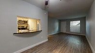 This single-story, one-bedroom, one-bathroom unit offers a practical and well-organized layout across a modest footprint. Wood-style plank flooring runs throughout the main living areas, providing a cohesive and easy-to-maintain surface. The open living area is illuminated by natural light from a front-facing window and is equipped with a ceiling fan, contributing to a comfortable, functional atmosphere.

The kitchen is designed as a galley-style space featuring white cabinetry, dark countertops, a white subway tile backsplash, a stainless steel sink, and stainless steel appliances including a refrigerator, range, and microwave. A pass-through window with a bar-height counter connects the kitchen to the living area, enhancing the sense of openness between the two spaces.

The bedroom offers a quiet retreat with a ceiling fan, continued wood-style flooring, and a reach-in closet with double doors and a hanging rod for clothing storage. The full bathroom includes a tub-shower combination with white tile surround, a toilet, and wood-style flooring. The unit's neutral gray walls and clean white trim create a consistent, understated aesthetic throughout.