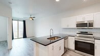 Located at 1200 E 15th St in Plano, TX, this one-bedroom, one-bathroom unit offers a thoughtfully designed layout with modern finishes throughout. Light wood-style flooring runs seamlessly across the entire space, creating a bright and cohesive aesthetic.

The kitchen is a standout feature, showcasing white shaker-style cabinetry, dark countertops, a light blue subway tile backsplash, and a full suite of stainless steel appliances including a French door refrigerator, range with microwave above, and dishwasher. A peninsula with an integrated sink provides additional prep space and a natural division between the kitchen and living area. Recessed lighting illuminates the space effectively.

The bedroom is a comfortable, light-filled room with a ceiling fan and a window offering views of surrounding greenery. A closet area within the bedroom conveniently houses a stacked washer and dryer unit, adding practical in-unit laundry functionality.

The bathroom is clean and well-appointed, featuring white subway tile surrounding a full soaking tub and shower combination, a white vanity with dark countertop, and the same light wood-style flooring carried throughout the unit. The overall design palette — whites, light wood tones, and dark countertop accents — gives the space a fresh, contemporary feel.