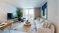 Located in the heart of Brickell at 77 SE Fifth Street, this elegantly designed two-bedroom, two-bathroom residence offers a refined urban living experience with sweeping views of the Miami skyline and Biscayne Bay. The open-concept living room is bathed in natural light from expansive floor-to-ceiling windows, framing breathtaking city and water vistas. The space is anchored by a neutral palette accented with bold blue artwork, creating a coastal-contemporary ambiance.

The chef's kitchen features light wood cabinetry with integrated under-cabinet lighting, a striking marble slab backsplash, sleek white countertops, brass fixtures, and a central island with bar seating — ideal for both casual dining and entertaining.

The primary bedroom is a serene retreat with textured accent wallcovering, decorative wall art, and soft layered bedding. The second bedroom benefits from generous natural light and direct city views through large windows. A dedicated closet provides ample storage.

Both bathrooms are finished with warm wood floating vanities, white countertops, gold-tone hardware, and large-format tile flooring. The primary bath features an elongated double vanity and a clean, spa-inspired aesthetic. Throughout the residence, light tile flooring, recessed lighting, and a cohesive warm-neutral design language create a polished, tranquil atmosphere.