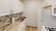 This single-floor space offers a practical and well-organized layout across several rooms, each designed for comfort and functionality. The kitchen stands out with its updated white cabinetry, granite-style countertops, a mosaic tile backsplash, a double-basin stainless steel sink, and hardwood-style flooring — giving the space a modern, clean aesthetic. White appliances, including a full-size refrigerator, complete the kitchen's functional appeal.

The living area transitions between carpet and hardwood-style flooring, creating distinct zones within an open feel. A ceiling fan provides both lighting and air circulation, while a front entry door adds a welcoming touch. The bedrooms are carpeted and bright, each equipped with ceiling fans and baseboard heating. One bedroom features a walk-in closet, offering generous storage. Windows with blinds allow natural light to filter in while maintaining privacy.

The bathroom is finished with classic white subway-style wall tiles surrounding a full soaking tub and shower combination, complemented by chrome fixtures for a timeless look. Throughout the space, neutral wall tones, baseboard heating, and consistent trim details create a cohesive and move-in-ready environment suitable for a range of occupants.