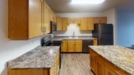Located at 4482 47th St S in Fargo, North Dakota, this single-floor unit offers a well-designed layout with functional living spaces throughout. The kitchen is a standout feature, showcasing warm honey-toned cabinetry, granite-style countertops, a central island, and a full suite of stainless steel appliances including a refrigerator, dishwasher, range, and microwave. Durable wood-look vinyl flooring runs through the kitchen and living areas, adding a clean, cohesive aesthetic. The open living room is bright and airy, highlighted by large sliding glass doors with vertical blinds that invite natural light and provide access to the outdoors. Bedrooms are carpeted for comfort and include windows that bring in additional natural light, with one bedroom featuring a ceiling fan. Closet space is well-represented, including a mirrored sliding-door closet in one room. The bathroom is finished with matching cabinetry, granite-style countertops, a vanity with ample storage, and a full bathtub. Textured ceilings are consistent throughout, and baseboard heating is present in multiple rooms. The overall layout is practical and efficiently organized, making this a comfortable and move-in ready space in south Fargo.