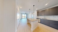 This contemporary 2-bedroom, 2-bathroom unit at 3930 Paradise Rd in Las Vegas offers a well-designed open-concept layout with modern finishes throughout. The kitchen is a standout feature, showcasing sleek gray cabinetry, a striking geometric herringbone tile backsplash, stainless steel appliances, and a central island topped with a neutral quartz surface — illuminated by stylish globe pendant lights. Light wood-style flooring runs through the main living area, which opens to a floor-to-ceiling glass sliding door, flooding the space with natural light and offering views of the Las Vegas skyline. A ceiling fan anchors the living area, adding both function and style. Both bedrooms are carpeted and bright, with large windows that frame outdoor views and allow ample natural light. The primary bedroom is generously sized with dedicated closet space. The two bathrooms maintain the unit's clean, modern aesthetic, featuring gray floating vanities with quartz countertops, subway-tiled shower surrounds, and glass-enclosed tub-shower combinations with polished chrome fixtures. Two closets provide practical storage throughout. The overall ambiance is clean, bright, and contemporary — ideal for modern urban living in the heart of Las Vegas.
