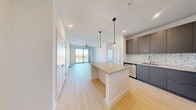 This contemporary 2-bedroom, 2-bathroom unit at 3930 Paradise Rd in Las Vegas offers a well-designed open-concept layout with modern finishes throughout. The kitchen is a standout feature, showcasing sleek gray cabinetry, a striking geometric herringbone tile backsplash, stainless steel appliances, and a central island topped with a neutral quartz surface — illuminated by stylish globe pendant lights. Light wood-style flooring runs through the main living area, which opens to a floor-to-ceiling glass sliding door, flooding the space with natural light and offering views of the Las Vegas skyline. A ceiling fan anchors the living area, adding both function and style. Both bedrooms are carpeted and bright, with large windows that frame outdoor views and allow ample natural light. The primary bedroom is generously sized with dedicated closet space. The two bathrooms maintain the unit's clean, modern aesthetic, featuring gray floating vanities with quartz countertops, subway-tiled shower surrounds, and glass-enclosed tub-shower combinations with polished chrome fixtures. Two closets provide practical storage throughout. The overall ambiance is clean, bright, and contemporary — ideal for modern urban living in the heart of Las Vegas.