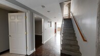 Located at 1429 Park St in Hartford, CT, this two-floor urban loft showcases a compelling mix of industrial heritage and contemporary design. The lower level features a wide corridor with dark hardwood floors, recessed lighting, and classically trimmed doorways that open to versatile rooms with clean grey walls and stained concrete flooring. Large multi-pane windows flood the entry and common areas with natural light, while an exposed brick accent wall adds raw, historic character. A staircase with a warm wood handrail connects the two floors, maintaining an open, flowing feel throughout. The well-appointed kitchen features rich wood cabinetry, dark granite countertops, a checkered tile floor, and a full suite of stainless steel appliances including a range, microwave, refrigerator, and dishwasher. The upper level reveals soaring exposed concrete ceilings with visible ductwork and structural columns — hallmark loft details that lend an authentic industrial aesthetic. The bathroom is distinctively designed, featuring a tiled soaking tub, warm hardwood floors, and a striking wall-mounted glass sink vanity with chrome hardware. A spacious walk-in closet with wire shelving provides ample storage. Throughout both floors, the interplay of concrete, brick, hardwood, and modern finishes creates a bold, architecturally rich environment.
