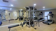 This dedicated fitness center offers a comprehensive workout environment designed to support a full range of exercise routines. The space is anchored by a professional-grade Life Fitness multi-station cable and strength training system, providing users with extensive options for resistance and functional training. Complementing the strength equipment, a treadmill and additional cardio machines are positioned to one side, catering to endurance and cardiovascular fitness needs. The flooring features durable rubber fitness tiles, offering both cushioning and traction during workouts. Full-length mirrors line one wall, enhancing the sense of space while allowing users to monitor their form. Recessed lighting in the ceiling provides bright, even illumination throughout the room. The neutral-toned walls and clean layout give the space a functional yet polished appearance. The overall design prioritizes practicality and accessibility, with equipment arranged to allow comfortable movement between stations. Whether for strength training, cardio, or functional fitness, this well-appointed gym delivers a versatile and professional exercise environment.