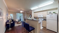 Located at 2725 E Lookout Dr in Garland, Texas, this multi-level residence spans three floors connected by carpeted stairs with a white handrail. The layout offers a well-organized flow between living, sleeping, and storage areas.

The main living level features an open-concept design where the kitchen connects seamlessly to the living and dining areas. The kitchen is equipped with light wood cabinetry, dark countertops, a breakfast bar with seating, and white appliances. Rich hardwood-style flooring runs throughout this level, complementing the warm neutral tones on the walls. Crown molding adds a refined architectural detail. The living area centers around a tile-surround fireplace and includes sliding glass doors that open to an outdoor balcony, allowing ample natural light and tree-lined views.

Two bathrooms feature tub-shower combinations, wood cabinetry with granite-style countertops, and hardwood-style flooring. The bedrooms are carpeted and showcase notable vaulted ceilings, which lend a sense of height and openness. One bedroom includes large windows with outdoor views, while another features an angled ceiling accent wall.

A lower-level storage area offers a concrete floor and wire shelving along multiple walls, providing generous organizational space.