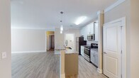 Located at 4020 St Croix Ln in Mebane, NC, this single-floor residence offers a thoughtfully designed layout with modern finishes and a cohesive, neutral color palette throughout. The open-concept kitchen serves as the heart of the home, showcasing crisp white shaker-style cabinetry, granite countertops, and a full suite of stainless steel appliances including a refrigerator, electric range, and built-in microwave. A central island with a sink and pendant lighting above adds both functionality and style, flowing seamlessly into the living area. Light wood-tone luxury vinyl plank flooring extends through the main living spaces, complemented by clean white trim and crown molding details. The bedroom features plush carpet, a ceiling fan, a window with natural light, and access to a spacious closet with built-in wire shelving. The bathroom is finished with tile flooring, a granite-topped vanity with undermount sink, and a full tub-shower combination. A dedicated laundry area with wire shelving and washer/dryer hookups adds convenience. The entry foyer features an elegant arched white door and hardwood-style flooring, creating a welcoming first impression. This residence combines practical living with clean, contemporary design.