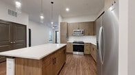 Located at 1400 Henderson Street in Fort Worth, Texas, this well-appointed one-bedroom, one-bathroom residence offers a thoughtfully designed single-level layout. The open-concept kitchen and living area serves as the heart of the home, showcasing warm wood-toned cabinetry, a crisp white quartz kitchen island with pendant lighting overhead, and a full suite of stainless steel appliances including a refrigerator, range, microwave, and dishwasher. A white subway tile backsplash and wood-look flooring throughout the main living areas add to the contemporary aesthetic. The living room is bright and airy, with a ceiling fan, large windows that invite natural light, and a glass-paneled door leading to a private patio. The bedroom features plush carpeting, a generously sized window with outdoor views, and direct access to a dedicated closet. The bathroom is finished with wood-toned vanity cabinetry and durable wood-look flooring, with a convenient pass-through to the closet. Additional spaces include a pantry, laundry area, and utility room, ensuring practical storage and functionality throughout. Clean white walls and dark baseboards create a polished, modern contrast across the entire residence.
