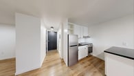 Located at 111 Porter Ave in Buffalo, NY, this single-floor unit offers a clean, modern aesthetic defined by a bright white palette and warm light wood flooring that runs continuously throughout the space. The layout is efficiently organized, with a well-appointed kitchen serving as a central feature. White shaker-style cabinetry, stainless steel appliances — including a full-size refrigerator and a range — and a dark-topped kitchen island provide ample prep and storage space, making the kitchen both functional and visually striking. A dedicated dining or flex area sits adjacent to the kitchen, offering flexibility for a variety of uses. The open entry corridor connects the living areas to a separate, generously sized room featuring a window with natural light and a baseboard heating unit, suitable for use as a bedroom or living space. Recessed and surface-mounted ceiling lighting provides consistent illumination throughout. The unit's crisp white walls and clean lines contribute to a minimalist, move-in-ready atmosphere. The space is well-suited for those seeking a practical, updated living environment in the Porter Avenue neighborhood of Buffalo's West Side.