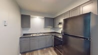 This single-floor, one-bedroom, one-bathroom residence in Saginaw, Michigan is thoughtfully laid out to maximize functionality and comfort. Throughout the unit, wood-look luxury vinyl plank flooring in a warm gray tone provides a cohesive, modern aesthetic.

The kitchen is well-equipped with gray shaker-style cabinetry, dark countertops, a double-basin sink, and black appliances including a refrigerator, range, and over-the-range microwave. The L-shaped layout offers ample counter and storage space for everyday use.

The living area features neutral gray walls accented by white wainscoting panel molding along the lower half, adding a classic architectural detail to the space. Natural light filters in through the windows, creating a bright and welcoming atmosphere.

The bedroom is comfortably sized with two windows fitted with vertical blinds, baseboard heating, and easy access to the full bathroom. A hallway with a closet connects the bedroom to the rest of the unit, providing convenient storage.

The bathroom is finished with a full tub and shower combination adorned with elegant marble-look tile surround featuring gray and gold veining. Wood-look flooring, a window for natural light, and clean white fixtures complete the space. Overall, the unit presents a clean, updated interior well-suited for comfortable single-floor living.