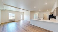Located at 2450 1st St SE in East Wenatchee, WA, this well-designed single-floor, 3-bedroom, 2-bathroom home offers a clean, modern aesthetic throughout. The open-concept living and kitchen area serves as the heart of the home, featuring light-toned luxury vinyl plank flooring, recessed lighting, and a bright, airy atmosphere created by neutral white walls and abundant natural light. The kitchen is well-appointed with gray shaker-style cabinetry, white countertops, black appliances including a refrigerator, range, and over-the-range microwave, and a large peninsula island with a built-in sink — ideal for both meal prep and casual dining. The living area flows seamlessly from the kitchen, offering a spacious and versatile layout. The bedrooms are carpeted and generously sized, with the primary bedroom featuring vaulted ceilings and a walk-in closet with built-in shelving. Additional bedrooms offer windows with scenic mountain views. A dedicated utility room houses in-unit laundry. The bathrooms are clean and functional, with one featuring a full tub-shower combination. The home's single-floor design, open layout, and modern finishes make it a comfortable and practical living space.