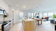 Located at 1240-1250 Cummings Ave in Ottawa, this modern 2-bedroom, 1-bathroom unit offers a well-designed open-concept layout with contemporary finishes and abundant natural light. Light-toned hardwood flooring flows seamlessly throughout the space, complementing the clean white walls and modern aesthetic.

The combined kitchen and living area serves as the heart of the unit. The kitchen features a central island with a white quartz countertop and an undermount sink with a matte black faucet, warm wood lower cabinetry, white upper cabinets, a white tile backsplash, and stainless steel appliances including a refrigerator, range, and built-in microwave. Large floor-to-ceiling windows bathe the open dining and living areas in natural light while offering expansive views of the Ottawa skyline.

The bathroom is finished with large-format marble-effect tile flooring, a floating vanity, a glass-enclosed walk-in shower, and an in-unit stacked washer and dryer for added convenience.

Both bedrooms are bright and well-proportioned, each featuring large windows with panoramic city views. The primary bedroom offers a comfortable footprint with ample natural light. A welcoming hallway with a dedicated closet and a stylish entryway with a circular mirror complete this thoughtfully designed home.