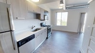 This single-story, one-bedroom, one-bathroom unit offers a contemporary design highlighted by light wood-style flooring that runs throughout the space. The open-concept layout connects the kitchen and living area seamlessly, creating a functional and airy atmosphere. Exposed silver ductwork along the ceiling adds an industrial design element that complements the modern aesthetic.

The kitchen is outfitted with light wood-grain cabinetry, white quartz countertops, and a full suite of stainless steel appliances, including a refrigerator, electric range, over-the-range microwave, and dishwasher. A dedicated pantry closet provides additional storage directly off the kitchen.

The living area benefits from generous natural light through large windows and a sliding glass door that opens to a private balcony with open city views. The bathroom features a walk-in shower, a single-sink vanity with light wood cabinetry and white countertop, built-in open shelving for storage, and wood-style flooring. A dedicated laundry closet houses a stacked GE washer and dryer unit alongside additional shelving, offering practical in-unit convenience. The bedroom includes a walk-in closet with wire shelving and hanging rods.