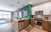 This 2-bedroom, 2-bathroom residence at 21 Quarry On offers a thoughtfully designed single-floor layout with contemporary style and vibrant character. The open-concept kitchen anchors the living space, featuring a peninsula with a white quartz countertop, dual pendant lights, stainless steel appliances, a subway tile backsplash, and a striking combination of white upper cabinets and warm wood-toned lower cabinetry set against a bold teal accent wall. Light hardwood-style flooring extends through the main living areas, complementing the airy, modern aesthetic.

The living room makes a bold statement with a deep charcoal feature wall, geometric wood artwork, and an open connection to the kitchen and entry. Natural light filters in through windows that offer views of surrounding greenery. Both bedrooms are carpeted and generously sized, with large windows providing additional natural light. The primary bedroom connects directly to a well-finished bathroom featuring warm wood vanity cabinetry and a glass-enclosed walk-in shower with neutral tile surround. The second bathroom includes a soaking tub and matching wood vanity. The second bedroom functions flexibly as a home office or guest space, benefiting from bright window views and ample room.