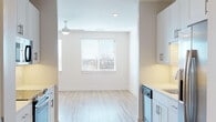This thoughtfully designed single-floor studio offers a clean, modern aesthetic with a bright and airy atmosphere throughout. The open-concept layout seamlessly connects the kitchen and living area, creating a functional and efficient use of space. Light wood-style flooring runs continuously throughout, contributing to the warm, cohesive feel of the interior.

The kitchen is well-appointed with crisp white shaker-style cabinetry, stainless steel appliances including a range and over-the-range microwave, and a textured tile backsplash that adds a subtle decorative touch. Light-toned countertops and under-cabinet lighting complete the polished look.

The main living area is generously proportioned, featuring recessed lighting and a ceiling fan that doubles as a light fixture. Large windows fitted with horizontal blinds allow abundant natural light to fill the room while offering outdoor views, enhancing the sense of openness.

The bathroom is clean and contemporary, featuring a wide white vanity with ample drawer storage, brushed nickel hardware, a large mirror, and warm wood-style flooring that ties seamlessly into the rest of the unit. The overall design maintains a neutral, minimalist palette of whites and soft grays, making the space feel bright, versatile, and move-in ready.