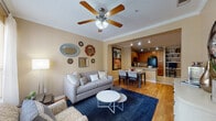 This single-floor residence offers a thoughtfully designed layout that seamlessly connects the main living areas. The living room serves as the central gathering space, featuring warm hardwood flooring, crown molding, a ceiling fan with light fixture, and a large window that invites natural light. A decorative wall arrangement of assorted mirrors adds a stylish focal point to the room.

The dining area flows directly from the living room and sits adjacent to the kitchen, separated by a granite-topped breakfast bar that doubles as additional counter space. The kitchen is equipped with warm oak cabinetry, granite countertops, tile flooring, and black appliances including a range, microwave, and refrigerator. Track lighting overhead provides functional illumination throughout.

The residence includes two bedrooms, each finished with plush carpeting, ceiling fans, and windows with sheer curtains that allow soft natural light. Both rooms offer a calm, restful ambiance with neutral tones throughout.

The full bathroom features tile flooring, a tub-shower combination, a broad vanity with granite countertops, warm wood cabinetry, and a large mirror with overhead lighting — providing ample storage and functionality. Overall, the space maintains a cohesive, neutral palette that creates a comfortable and inviting atmosphere throughout.