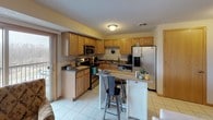 This single-floor residence offers a thoughtfully designed layout with a range of comfortable living spaces. The kitchen is well-equipped with warm oak cabinetry, dark granite-style countertops, black and stainless steel appliances including a built-in microwave, electric range, dishwasher, and refrigerator with ice dispenser. A central island with a butcher block top and bar seating provides additional prep space and casual dining. Light tile flooring and a sliding glass door bring brightness to the kitchen area.

The living room is an inviting space with large sliding glass doors that open to a balcony, flooding the room with natural light and offering outdoor views. A textured ceiling adds architectural character throughout the home.

The primary bedroom features plush carpeting, a walk-in closet, and ample room for furnishings. A second bedroom is carpeted and includes a window with natural views, while a third flexible room with direct balcony access serves well as a home office or guest space.

Two full bathrooms are finished with wood-toned cabinetry and white countertops. One features a shower-tub combo with sliding glass doors, while the other includes a standalone walk-in shower, also with sliding glass enclosure. Both are finished with tile flooring for easy maintenance.
