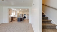 This two-story home is designed with a clean, modern aesthetic and a practical layout that flows naturally between living and functional spaces. The main level centers around an open-concept kitchen and living area. The kitchen is well-equipped with stainless steel appliances, including a refrigerator, range, and over-the-range microwave. Light-toned shaker-style cabinetry extends to the ceiling for ample storage, and a white subway tile backsplash adds a classic touch. A center island with a dark base and light countertop provides additional workspace and serves as a visual anchor. Light wood-look tile flooring runs throughout the kitchen, transitioning to soft carpet in the adjacent living area. A carpeted staircase leads to the upper level, where the bedrooms offer plush carpet, natural light from windows with blinds, and ceiling fans for comfort. The bathrooms are finished with large-format white tile flooring and full soaking tub-shower combinations. A dedicated laundry room on the upper level includes a full-size washer and dryer with overhead shelving. Throughout, the home maintains a neutral, light-filled palette with white walls and recessed lighting.