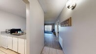 Located at 3830 University Center Drive in Las Vegas, NV, this 2-bedroom, 1-bathroom unit offers a practical and well-organized single-floor layout. The entryway, finished with light tile flooring, opens into a combined kitchen and living area. The kitchen features white cabinetry, a pass-through breakfast bar, and under-cabinet lighting, making it both functional and open to the dining and living spaces. The living room is bright and airy, anchored by a large sliding glass door with vertical blinds that leads to a private balcony overlooking the Las Vegas skyline — a standout feature of the unit. Wood-style laminate flooring extends throughout the main living areas and bedrooms, providing a cohesive look. The primary bedroom is generously proportioned and includes its own dedicated closet, while the second bedroom is bright with a window fitted with vertical blinds and easy access to a shared closet. A hallway connects the bedrooms to the full bathroom, which features a wide vanity with a speckled countertop, ample mirror space, white cabinetry, and a tiled shower-tub combination. Textured ceilings are consistent throughout the unit, adding a classic residential character to the overall space.