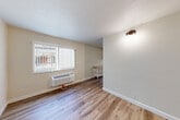 Located at 1229 Pacific Ave in Santa Rosa, CA, this efficient one-bedroom, one-bathroom unit is thoughtfully laid out across a single floor. The living room serves as the central gathering space, featuring light hardwood-style flooring, neutral warm-toned walls, a textured ceiling, and a large window fitted with vertical blinds that allows natural light to fill the room. A wall-mounted PTAC heating and cooling unit ensures year-round climate control. A wall sconce provides additional ambient lighting. The living area flows into a compact combined dining and kitchen space, complete with a wooden countertop work surface. A hallway connects the main living areas to the private bedroom, which is a cozy, well-defined space with the same consistent hardwood-style flooring and a wall sconce light fixture. The bathroom is a clean, well-appointed room featuring a full tub and shower combination framed by classic white subway tile, accented with a decorative mosaic tile border. A frosted window above the shower brings in natural light while maintaining privacy. Throughout the unit, the consistent flooring, neutral color palette, and clean finishes create a cohesive and functional living environment.
