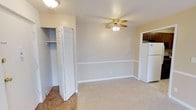 Located at 7191 Mentor Ave. in Mentor, Ohio, this single-floor space offers a straightforward and functional layout designed for comfortable everyday living. The floor plan reveals a well-organized arrangement of rooms, including defined living, sleeping, and utility areas that make efficient use of the available space.

The main living area features neutral-toned walls with a classic chair rail detail, soft carpeted flooring, and a ceiling fan with integrated lighting that provides both comfort and illumination. A closet with bifold doors and built-in shelving offers convenient storage directly off this space. Adjacent to the living area, the kitchen is equipped with a full-size refrigerator and cabinetry finished in a warm wood tone, providing practical storage and workspace.

The overall aesthetic throughout the unit is clean and understated, with white trim and baseboards, light-colored walls, and consistent flooring transitions between rooms. The layout as seen from the floor plan model indicates multiple separated rooms, allowing for clear distinctions between living, sleeping, and bathroom areas. The space presents a move-in-ready condition with a neutral palette that accommodates a variety of personal styles and furnishing preferences.
