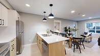 This thoughtfully designed single-floor unit offers 4 bedrooms and 3 bathrooms within a compact, efficiently utilized layout. The open-concept kitchen and living area serves as the heart of the home, featuring a central island with a white quartz countertop, stainless steel sink, and integrated dishwasher, complemented by light wood cabinetry with matte black hardware. Stainless steel appliances, including a freestanding range and refrigerator, are paired with full-height upper cabinets, maximizing storage. Pendant lighting with sleek black dome fixtures adds a modern touch overhead. The living area is bright and inviting, with large windows and a glass door providing natural light and outdoor access. A wall-mounted mini-split system ensures year-round comfort. Bedrooms are calm and understated, finished in a soft grey palette with light hardwood-style flooring and windows that bring in natural light. The primary bedroom includes a walk-in closet with wire shelving. The bathrooms are finished with white quartz vanity tops, light wood cabinetry, black-framed round mirrors, and glass-enclosed showers. Consistent use of light flooring, neutral grey walls, and black accents throughout creates a cohesive, contemporary aesthetic.