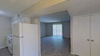This single-floor residence offers a clean, functional layout designed for comfortable everyday living. The open living and dining area is finished with light hardwood-style flooring and neutral gray walls, creating a bright, cohesive atmosphere. A sliding glass door with vertical blinds fills the living room with natural light and provides outdoor access, while a chandelier overhead adds a warm accent to the adjoining dining space.

The galley-style kitchen is efficiently organized with white cabinetry, light granite-look countertops, and matching white appliances, including an electric range. The layout maximizes storage and counter space along both walls, making it practical for everyday cooking.

The bedrooms are carpeted and finished in soft neutral tones, each featuring windows that bring in natural light. One bedroom offers a connected hallway leading to additional rooms or storage, adding to the overall flow of the unit. Textured ceilings are present throughout the home, consistent with the residential character of the space.

A hallway connects the private areas of the home, with a bathroom accessible along the corridor. The overall color palette — soft grays, warm beiges, and crisp whites — lends the space a clean, move-in-ready feel that is both practical and inviting.