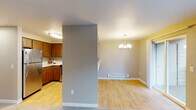 This single-floor unit is thoughtfully laid out with a functional open-concept design that connects the kitchen, dining, and living areas. A structural half-wall divides the kitchen from the dining space, which is anchored by a modern chandelier and equipped with a baseboard heater. Light wood-style flooring runs throughout the main living areas, contributing to a bright, cohesive aesthetic.

The kitchen features warm wood-toned cabinetry extending to the upper walls for ample storage, light-colored countertops, a stainless steel double-basin sink, an electric range, and a stainless steel refrigerator. A peninsula-style counter offers additional workspace and casual seating potential, opening toward the adjacent living area.

The bedroom is carpeted in neutral tones and includes a sliding-door closet and a window that allows natural light to filter in. A flush-mount ceiling fixture provides overhead lighting.

The bathroom is finished with wood-style vinyl flooring, taupe-painted walls, a vanity with under-sink cabinetry, a tub-shower combination with a curved curtain rod, and a grab bar for added accessibility. Overall, the unit presents a clean, practical living environment with consistent, neutral finishes throughout.