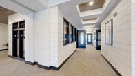 Located at 400 Oak Grove Pkwy in Vadnais Heights, MN, this thoughtfully designed single-floor amenity space offers a generous footprint across seven distinct areas, each finished with a cohesive modern-farmhouse aesthetic. The main corridors feature white shiplap wall paneling, dark-framed interior windows, and striking coffered ceilings with wood inlays, creating a polished and welcoming first impression throughout.

A stylish lounge area provides a comfortable retreat with light wood furnishings, large black-framed windows that invite abundant natural light and outdoor views of the surrounding greenery. Adjacent to it, a well-appointed kitchen showcases quartz countertops, warm wood cabinetry, and stainless steel appliances atop light hardwood flooring.

A bright dining area is anchored by floor-to-ceiling black-framed windows that frame views of the outdoor pool and landscaping, flooding the space with sunlight. Patterned area rugs, black horizontal railings, and wood-plank ceiling accents add character to the mezzanine-style gathering area nearby.

The fitness facilities are divided into two dedicated spaces: a cardio and strength training room outfitted with treadmills, ellipticals, free weights, and wall-mounted TVs, and a separate studio room with floor-to-ceiling mirrors and cycling equipment. Together, these amenity spaces deliver a refined, functional, and visually cohesive environment.