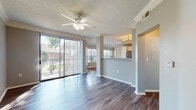 This single-floor residence offers a thoughtfully designed open-concept layout that balances comfort and functionality. The living area is a welcoming space, finished with rich hardwood-style flooring that flows throughout the main areas. A ceiling fan with integrated lighting adds both comfort and character, while crown molding lends a refined architectural detail. Large sliding glass doors with vertical blinds flood the living space with natural light and provide direct access to an outdoor area, offering pleasant views of the surrounding greenery.

The kitchen is a standout feature, equipped with stainless steel appliances including a refrigerator, range, and microwave. Crisp white cabinetry provides generous storage, while stone-look granite countertops add an elegant, durable surface. A curved breakfast bar peninsula connects the kitchen to the living area, making the space ideal for both meal preparation and casual dining.

The bedrooms are carpeted for warmth and comfort, each featuring a ceiling fan and windows that invite natural light. The layout provides a sense of privacy, with well-proportioned rooms suitable for a variety of uses. The bathroom includes a full soaking tub with a tiled surround, complemented by the same hardwood-style flooring found throughout the rest of the home. Neutral gray tones and textured ceilings are consistent throughout, creating a cohesive and modern aesthetic.