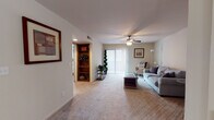 This single-floor residence offers a thoughtfully designed layout with a comfortable flow between living, dining, and sleeping areas. The living room is a welcoming space anchored by a tile-surround fireplace and fitted with plush carpeting, a ceiling fan, and wide sliding glass doors that invite natural light and provide access to the outdoors. Adjacent to the living room, the dining area features a tray ceiling detail that adds architectural interest, creating a defined and intimate space for meals. The kitchen is well-equipped with warm wood cabinetry, granite-style countertops, black appliances, and tile flooring, offering ample storage and workspace. A hallway with tile flooring connects the main living areas to the private quarters, where two bedrooms offer carpeted floors, ceiling fans, and natural light from slatted windows. Each bedroom provides a restful atmosphere with generous proportions. The two bathrooms are consistently finished with granite-topped wood vanities, tile surround tub-shower combinations, and tile flooring. Built-in shelving near the entry adds practical storage. Throughout the residence, neutral tones and consistent finishes create a cohesive and move-in-ready environment.
