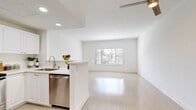 This single-floor residence is designed with a clean, modern aesthetic, featuring a crisp white palette and light wood-tone flooring that extends seamlessly throughout the entire space. The open-concept layout connects the kitchen and living area, creating a bright and airy atmosphere enhanced by natural light streaming through windows fitted with horizontal blinds.

The kitchen is well-appointed with white shaker-style cabinetry, light quartz countertops, recessed lighting, and a full suite of stainless steel appliances including a refrigerator, range, microwave, and dishwasher. A peninsula counter provides a natural divide between the kitchen and the spacious living area, which offers a comfortable sense of openness with views to the outdoors.

The bedrooms are generously proportioned, each featuring the same light wood flooring, white walls, and ample natural light. One bedroom includes a mirrored sliding-door closet that enhances the sense of space, while another features vaulted ceiling lines that add architectural interest.

The bathroom showcases a bright, functional design with a wide vanity, white cabinetry with brushed nickel hardware, a large mirror, and a window that brings in natural light. Overall, the space presents a well-maintained, move-in-ready interior with a cohesive and understated modern style.