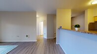 Located at 10906 E Portland Ave in Tacoma, Washington, this single-floor residence offers a well-organized layout with a clean, modern aesthetic. The living areas feature durable vinyl plank flooring in a warm wood tone, complemented by neutral gray and white walls that create a bright, open atmosphere. A bold yellow accent wall adds a touch of character near the kitchen pass-through, which features a granite-style countertop overhang ideal for casual dining.

The kitchen is efficiently designed in a galley style, outfitted with light maple cabinetry, granite-style countertops, tile backsplash, and stainless steel appliances including a refrigerator, electric range, and over-the-range microwave. Adjacent utility space provides additional storage and houses the water heater. The bedrooms are carpeted for comfort, with one room featuring a large picture window that frames views of mature evergreen trees and the surrounding neighborhood, along with a baseboard heater beneath. The bathroom is finished with matching light maple cabinetry, a granite-style vanity top, wood-look vinyl flooring, and a shower with curtain rod. Throughout, the space maintains a consistent, updated finish palette suited for comfortable everyday living.
