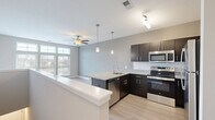 Located at 405 Smith Rd in West Chicago, IL, this two-floor unit offers a well-designed layout that maximizes its footprint across both levels. The main living area is anchored by a modern, open-concept kitchen that flows seamlessly into the living space. The kitchen is outfitted with dark espresso cabinetry, granite countertops, a subway tile backsplash, and a full suite of stainless steel appliances including a refrigerator, range, microwave, and dishwasher. A peninsula with an integrated sink and pendant lighting overhead serves as both a functional workspace and a natural divider between the kitchen and living areas. Light wood-style flooring runs throughout, complementing the neutral gray and beige wall tones. A ceiling fan with lighting anchors the living area, while large windows allow natural light to fill the space. The second level, accessed via an interior staircase, provides additional living space finished with the same light flooring and clean white trim. The bathroom features a soaking tub with a tiled shower surround and chrome fixtures. A closet offers convenient built-in storage. The overall aesthetic is clean, contemporary, and functional.