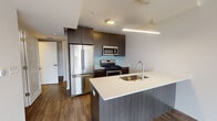 This thoughtfully designed single-floor residence offers a clean, contemporary aesthetic with quality finishes throughout. Warm hardwood-style flooring runs continuously across the open-concept living and dining areas, creating a cohesive and inviting atmosphere. Large windows flood the living spaces with natural light and offer views of the surrounding brick exterior architecture.

The kitchen is a standout feature, equipped with stainless steel appliances including a French-door refrigerator, gas range, and over-the-range microwave. Dark, wood-grain cabinetry provides ample storage, while a light aqua glass tile backsplash adds a vibrant accent. A central island with a white quartz countertop and undermount sink serves as both a prep space and a social hub. An in-unit stacked washer and dryer is conveniently accessible from the kitchen area.

The bedrooms are generously proportioned, each benefiting from natural light through large windows. One bedroom features elegant recessed cove lighting along the ceiling, adding a refined ambiance. A clean, well-lit entry corridor leads to the front door, providing a welcoming transition into the home.

The bathrooms are finished with large-format marble-look wall tiles in the tub-shower surrounds and neutral gray floor tiles, complemented by chrome fixtures and dark-toned vanity cabinetry, delivering a polished and modern look.