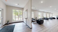 This expansive single-floor amenity facility offers a comprehensive range of shared spaces designed for comfort and active living. The welcoming lobby greets visitors with large floor-to-ceiling windows that flood the space with natural light, wood-look flooring, and a seating area furnished with dark leather chairs. Adjacent to the entry, a broad open common area managed by Connect Property Management features high-top bar seating, smooth hardwood-style floors, and branded wall art, with a vending machine adding everyday convenience. The lounge area transitions seamlessly from the common space, anchored by a wall-mounted flat-screen TV above a sleek linear fireplace, complemented by plush seating and neutral carpeting that creates a warm, inviting atmosphere. The fitness studio is well-appointed with herringbone-patterned flooring, a full-width wall mirror, stability balls, resistance equipment, free weights, and exercise mats — catering to a variety of workout routines. The indoor aquatic area stands out as a highlight, featuring a pool and spa with stainless steel entry rails, speckled concrete flooring, and full-length glass garage-style doors that open to an outdoor patio. Seating areas within the pool room allow for relaxation alongside the water. Throughout, the facility maintains a clean, modern aesthetic with recessed lighting, neutral tones, and thoughtful layouts.
