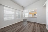 This two-bedroom, one-bathroom unit in Caldwell, Idaho offers a well-organized single-floor layout with wood-look flooring extending throughout every room. The open-concept living and kitchen area forms the heart of the unit, where a peninsula with a double-basin sink and light countertops separates the kitchen from the living space. The kitchen is equipped with warm honey-toned cabinetry, a white refrigerator, electric range, and built-in microwave, providing ample storage and functionality. The living room benefits from large windows fitted with white horizontal blinds, allowing generous natural light to fill the space, which features notably elevated ceilings that enhance its open feel. Both bedrooms are comfortably sized, each with wood-look flooring, neutral gray walls, and windows with blinds. The primary bedroom includes two closet doors and additional utility access. The full bathroom features a combined tub and shower with white tile surround, a vanity with warm wood cabinetry, and a window for natural light. A hallway connects the main living areas to the bedrooms and bathroom, completing the functional and cohesive layout of this Caldwell residence.