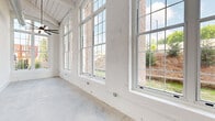 This thoughtfully designed one-bedroom, one-bathroom residence in Warrenville, SC offers a compelling blend of industrial character and modern finishes across a single, well-organized floor. The living area is a standout, defined by soaring ceilings with exposed ductwork and painted wood beam detailing, polished concrete floors, and a dramatic bank of oversized grid-pane windows that flood the space with natural light and frame views of the surrounding landscape. A ceiling fan with a sleek profile anchors the open living area, which flows seamlessly toward the private quarters. The galley-style kitchen is well-appointed with white shaker cabinetry paired with matte black hardware, granite countertops, a white subway tile backsplash, stainless steel appliances including a refrigerator, range, dishwasher, and microwave, as well as pendant lighting and an exposed structural wood post that nods to the building's heritage. The bedroom offers generous proportions, lofty ceiling height, and natural light from large windows. The bathroom features polished concrete flooring, a glass-enclosed walk-in shower with white tile surround, and matte black fixtures throughout, maintaining a cohesive modern-industrial aesthetic. This residence delivers a distinctive urban loft experience with refined, contemporary finishes.