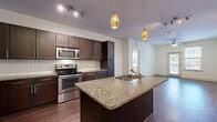 This thoughtfully designed 2-bedroom, 2-bathroom single-story residence offers a functional and stylish layout ideal for comfortable everyday living. The open-concept kitchen and living area serves as the heart of the home, showcasing rich dark espresso cabinetry, granite countertops, a subway tile backsplash, and a full suite of stainless steel appliances including a refrigerator, range, and built-in microwave. A central kitchen island with an integrated sink and elegant pendant lighting adds both practicality and visual appeal. Wood-style flooring flows seamlessly throughout the entire residence, contributing to a warm, cohesive aesthetic. The living area features a ceiling fan and access to a private outdoor space through a glass door, allowing natural light to fill the room. Both bedrooms are generously sized, each equipped with ceiling fans and windows that invite natural light. The primary bedroom connects to a well-appointed en-suite bathroom featuring a dual-sink granite vanity, a soaking tub, and a separate glass-enclosed shower. The secondary bathroom mirrors the same upscale finishes. Both bedrooms are complemented by spacious walk-in closets with wire shelving systems. A dedicated in-unit laundry room with full-size washer and dryer connections adds everyday convenience, completing this well-rounded residence.